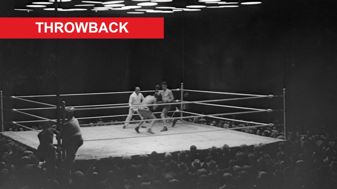 A wide shot of a boxing ring as Jack Dempsey boxes against Gene Tunney with a red rectangle labeled "Throwback" in the top left hand corner